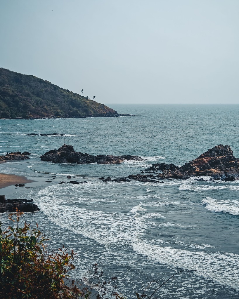 Rocky Goa coastline with teal waves and a green hillside